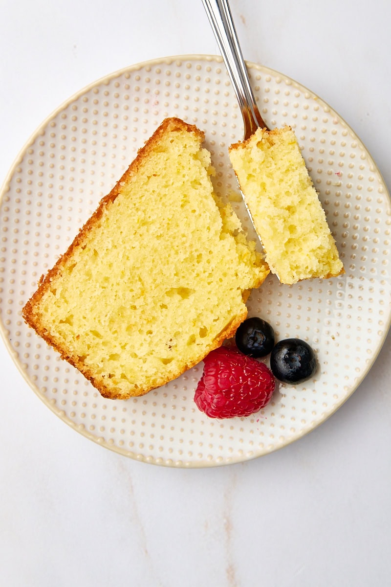 overhead view of a slice of yogurt cake on a plate with a bite on a fork resting on the plate