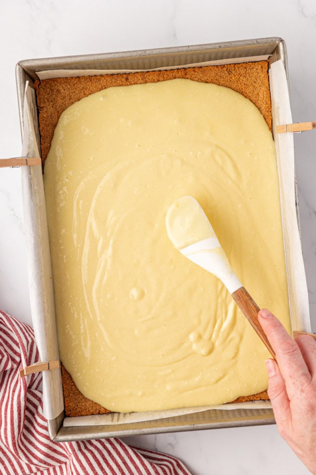 overhead view of cheesecake batter being spread over partially baked graham cracker crust