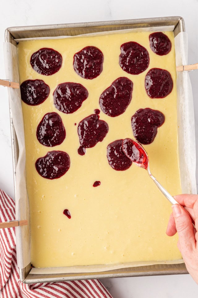 overhead view of cherry topping being spooned onto cheesecake batter