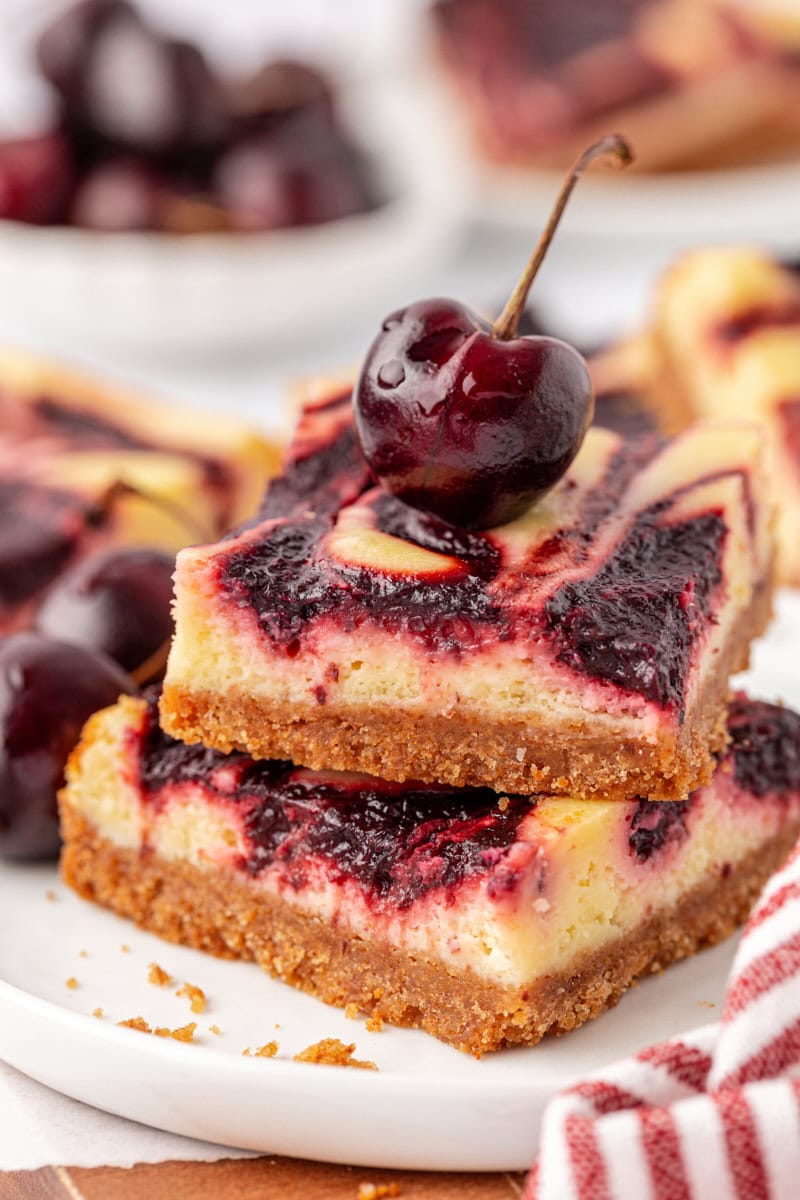 a stack of two cherry cheesecake bars with a fresh cherry on top