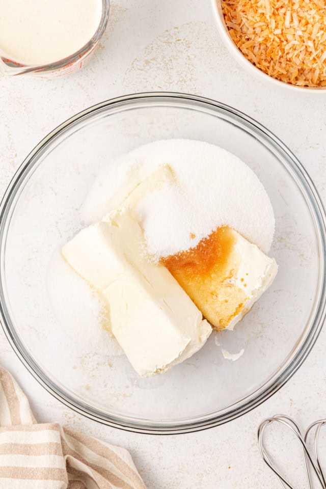 overhead view of cream cheese, sugar, and vanilla extract in a glass mixing bowl