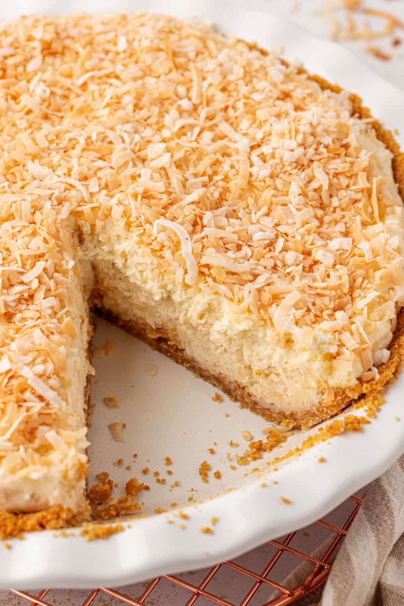 no-bake coconut cheesecake in a white pie plate with a slice removed