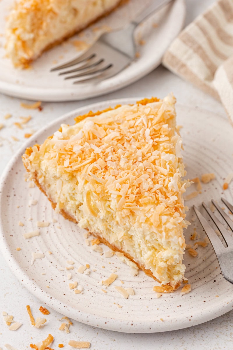 a slice of no-bake coconut cheesecake on a plate with another slice on a plate partially visible in the background