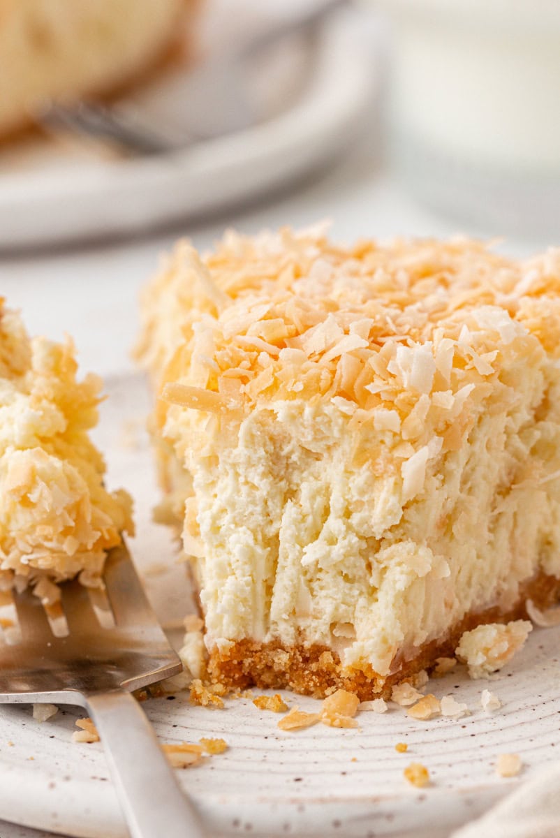 close-up of a slice of no-bake coconut cheesecake on a plate with a bite on a fork