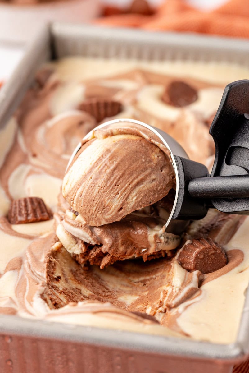 no-churn chocolate peanut butter ice cream in an ice cream scoop resting on the remaining ice cream in a metal loaf pan