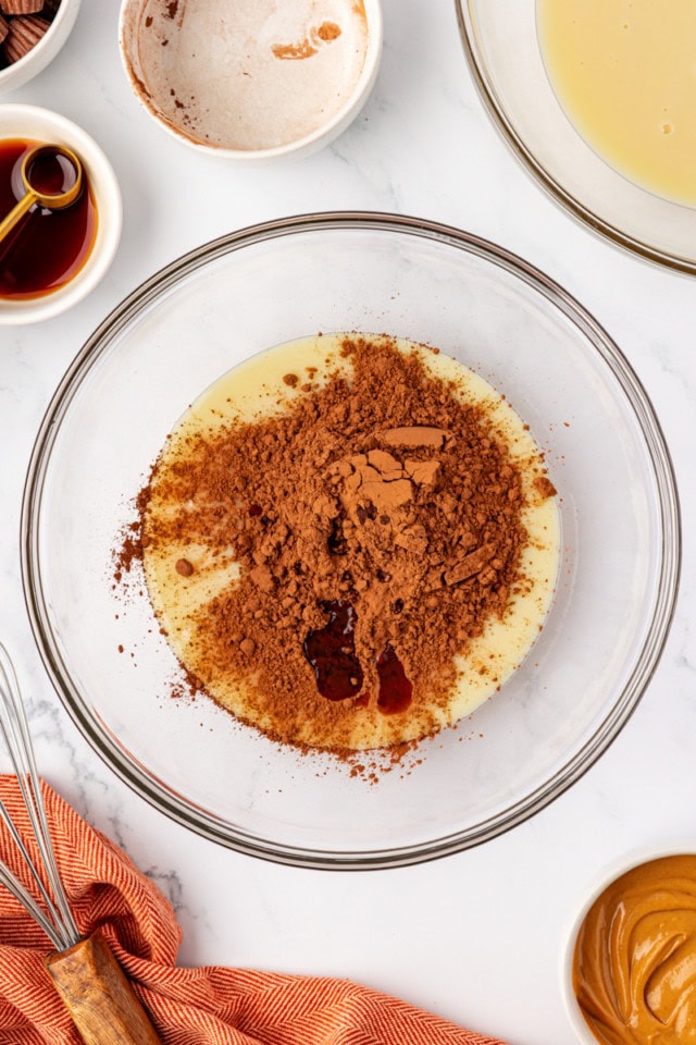 overhead view of cocoa powder and vanilla extract added to sweetened condensed milk in a glass mixing bowl