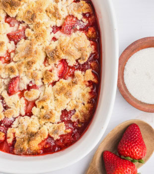 overhead view of strawberry cobbler in a white baking dish with fresh strawberries scattered beside the dish