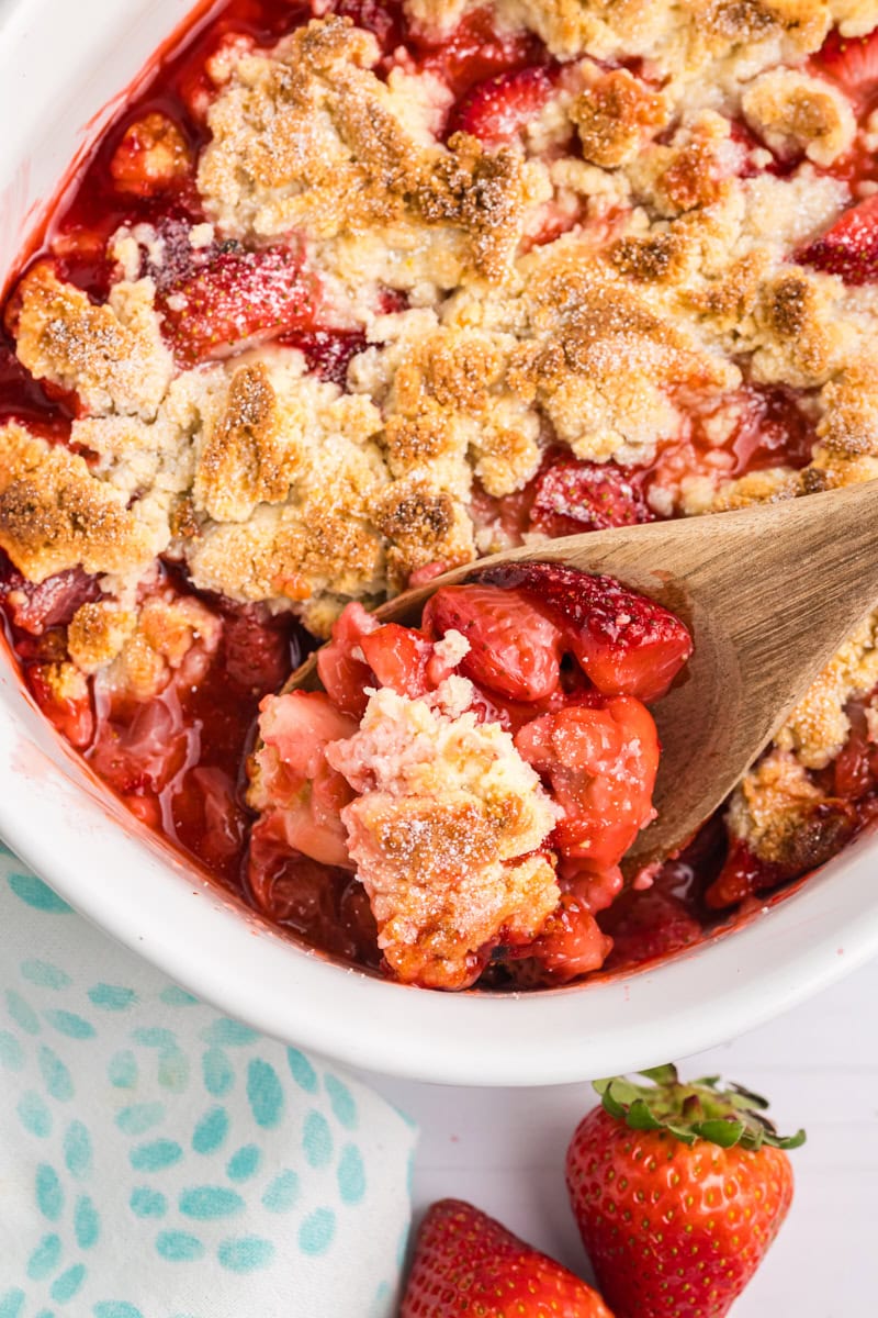 a spoonful of strawberry cobbler on a wooden spoon with the remaining cobbler in the background
