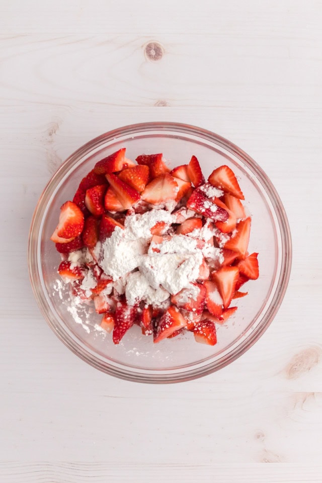 overhead view of strawberries, sugar, cornstarch, and lemon juice in a glass mixing bowl