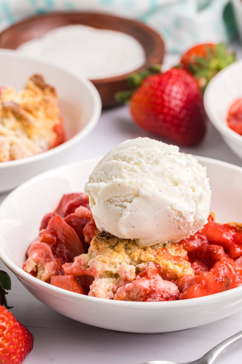 strawberry cobbler in a white bowl, topped with a scoop of vanilla ice cream