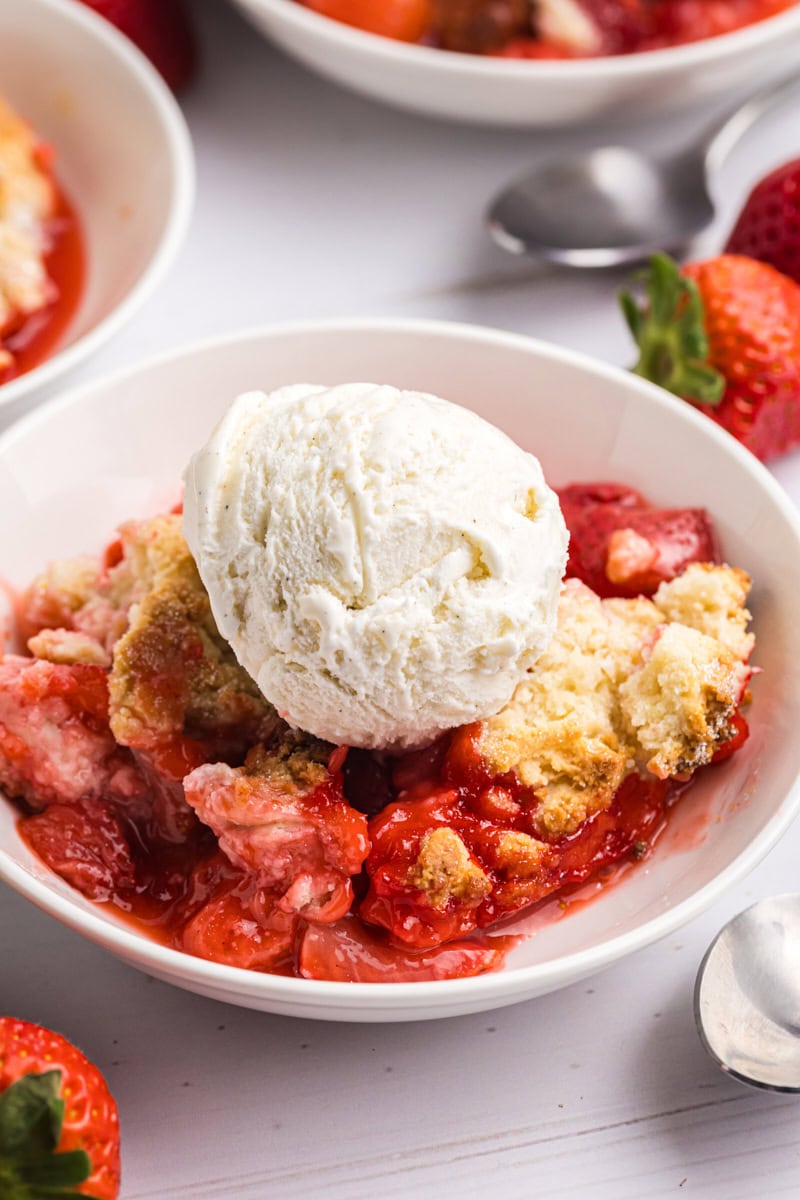 a bowl of strawberry cobbler topped with vanilla ice cream in a white bowl