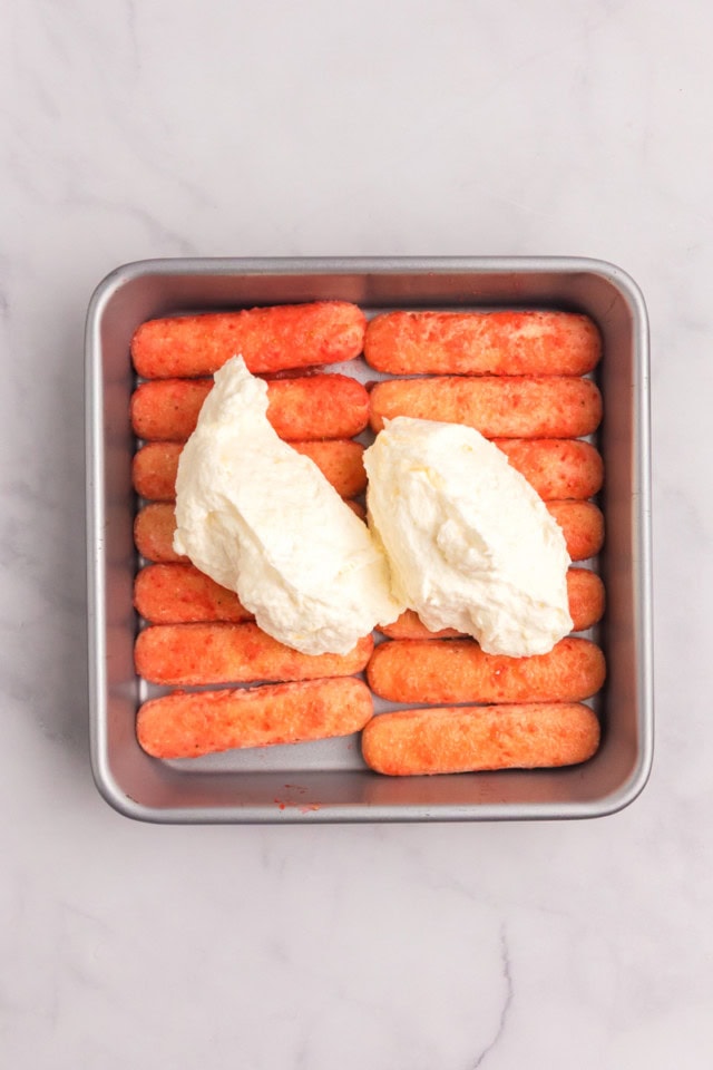 overhead view of strawberry-soaked ladyfingers in a square pan with mascarpone filling spooned on top