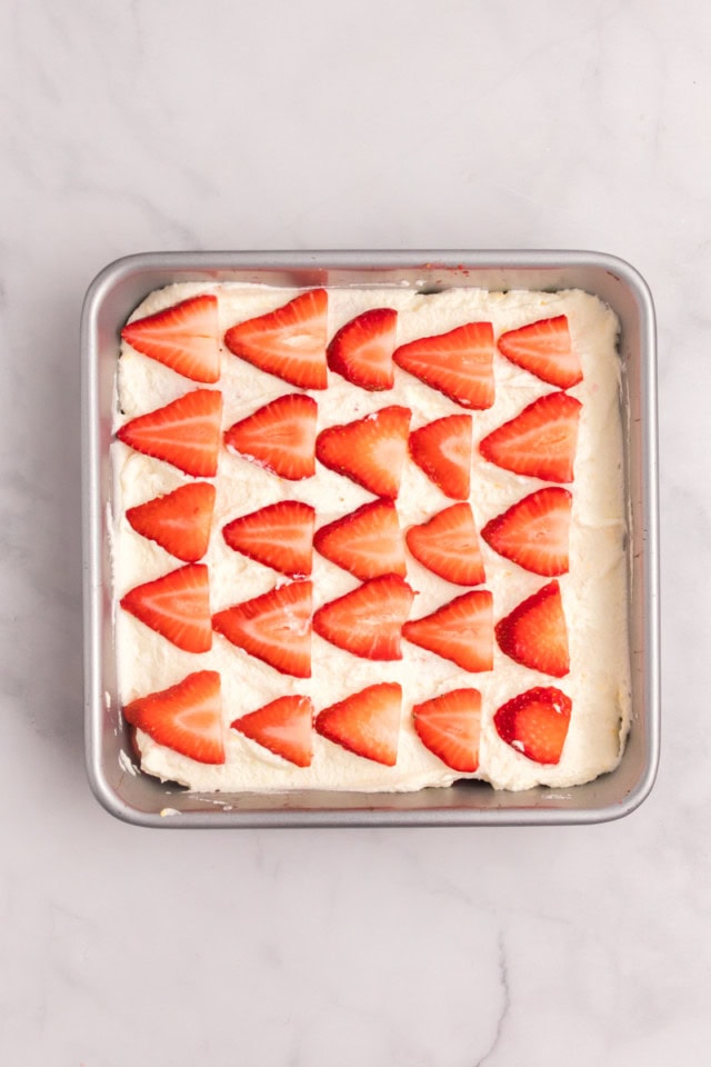 overhead view of the first layer of mascarpone filling and sliced strawberries for strawberry tiramisu in a square pan