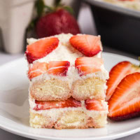 a slice of strawberry tiramisu on a white plate with sliced strawberries on the side