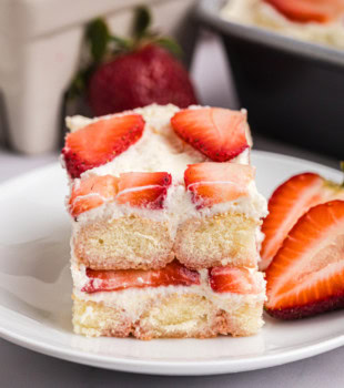 a slice of strawberry tiramisu on a white plate with sliced strawberries on the side