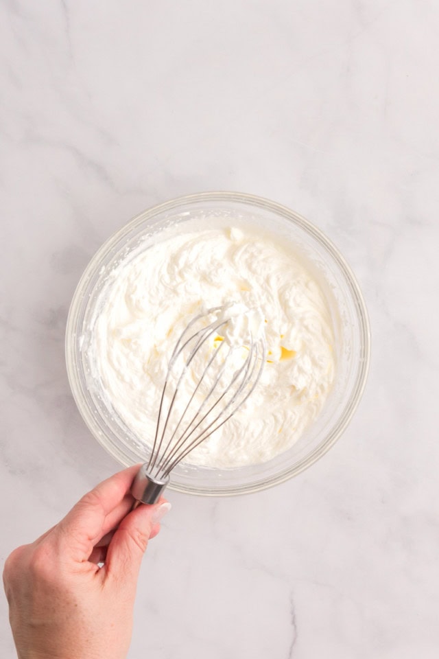 overhead view of whipped cream in a glass mixing bowl with a whisk held over it