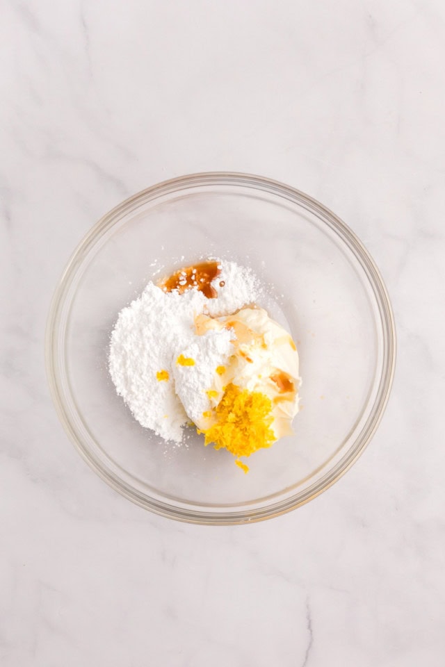 overhead view of mascarpone, confectioners' sugar, vanilla, and lemon zest in a glass mixing bowl