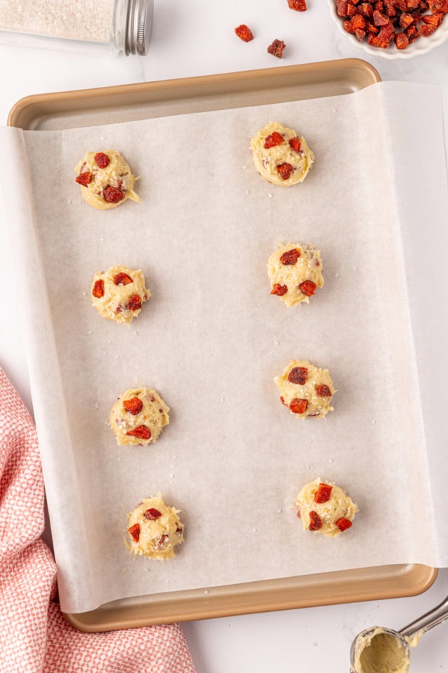 overhead view of portioned strawberry cream cheese cookie dough topped with more dried strawberries on a parchment-lined baking sheet 