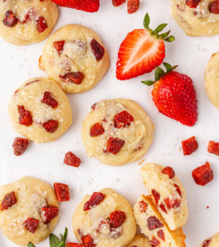 overhead view of strawberry cream cheese cookies scattered on a white surface with fresh strawberries