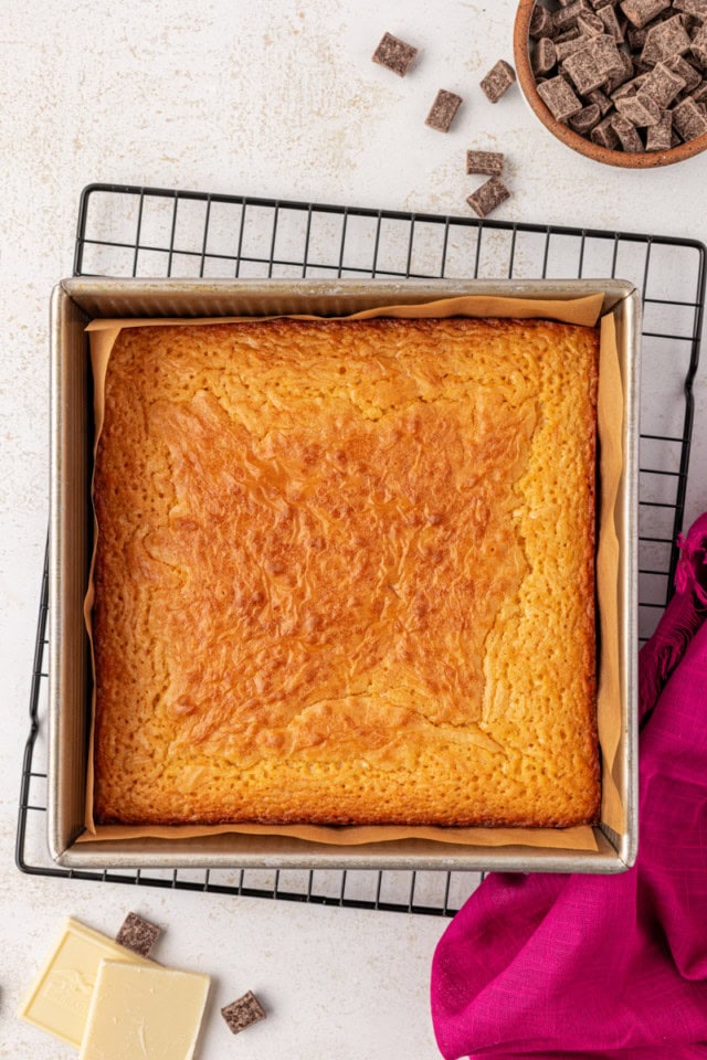 overhead view of freshly baked white chocolate brownies in a square baking pan on a wire rack