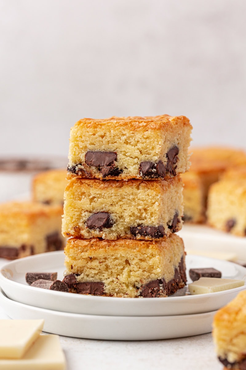 stack of three white chocolate brownies on a white plate with more brownies in the background