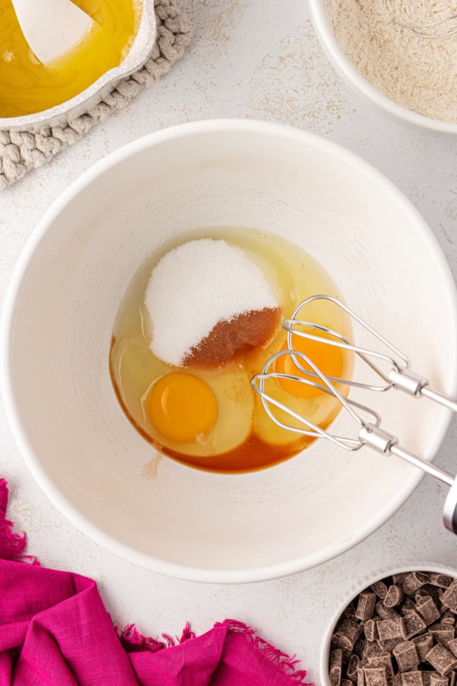 overhead view of eggs, sugar, and vanilla in a white mixing bowl
