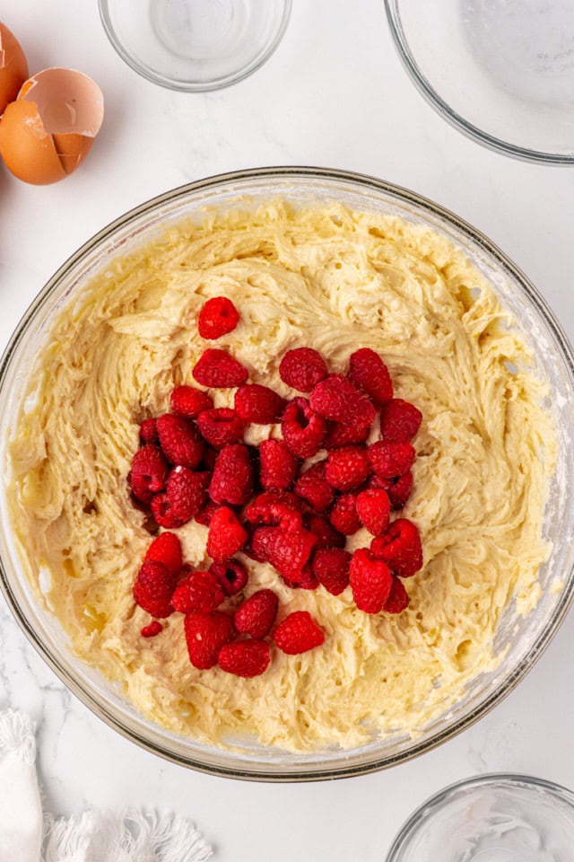 overhead view of raspberries added to cake batter in a glass mixing bowl