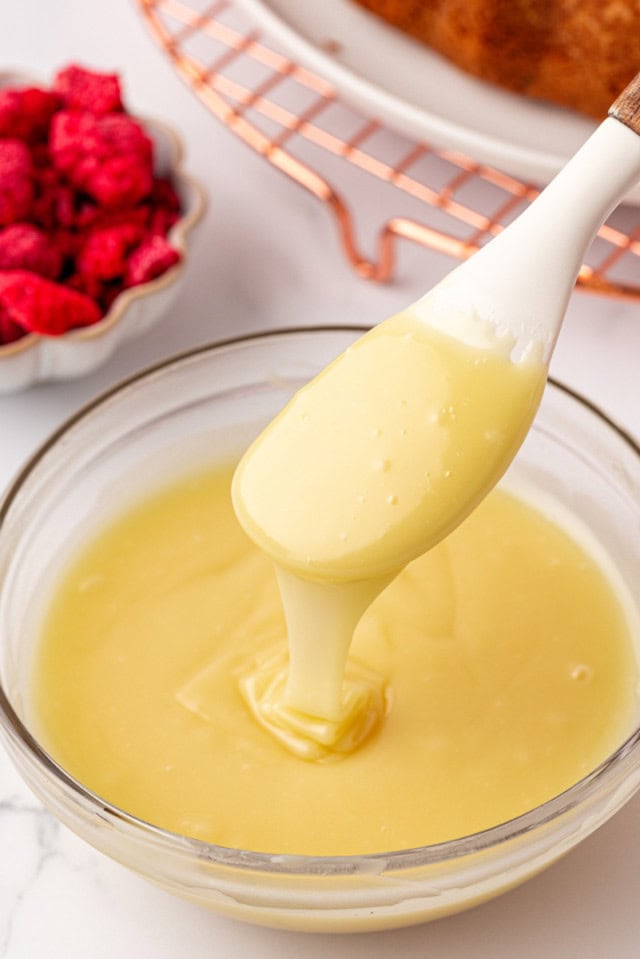 white chocolate ganache in a glass bowl with a spatula lifting out of the bowl