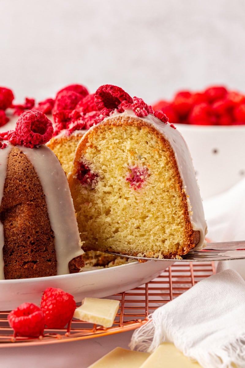 a slice of white chocolate raspberry Bundt cake on a cake server lifting away from the remaining cake