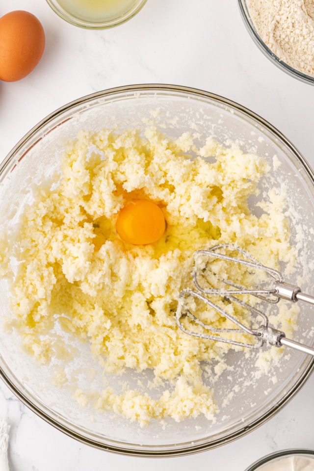 overhead view of egg added to creamed butter and sugar in a glass mixing bowl