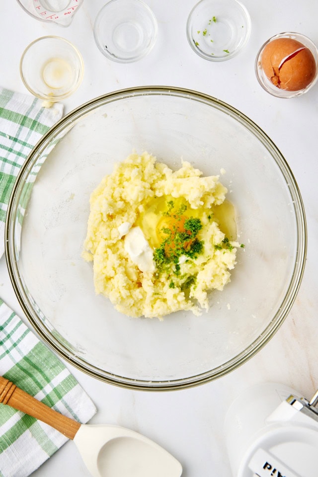 overhead view of sour cream, egg, lime zest, lime juice, vanilla extract, and coconut extract added to creamed butter and sugar in a glass mixing bowl