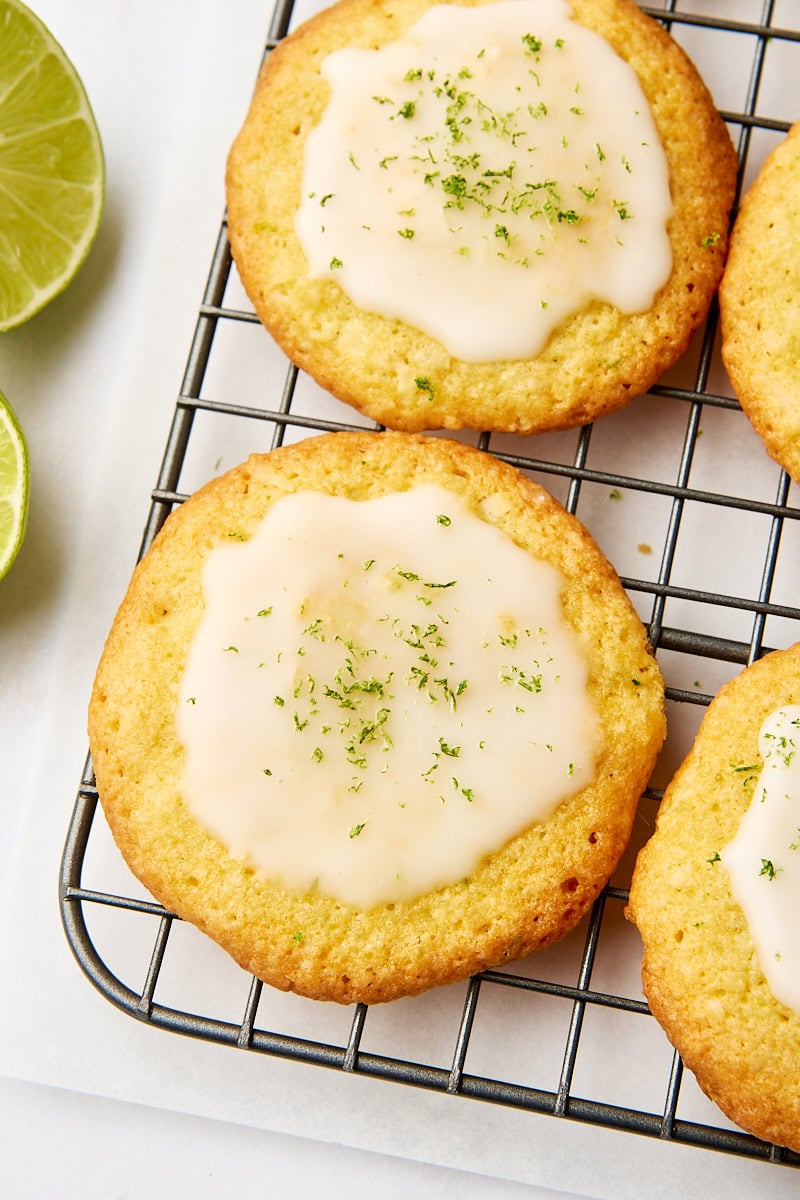 close-up view of a coconut lime cookie on a wire rack surrounded by more cookies and slices of lime