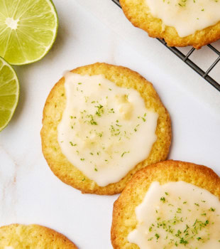 overhead view of two coconut lime cookies on a white surface surrounded by more cookies and lime slices