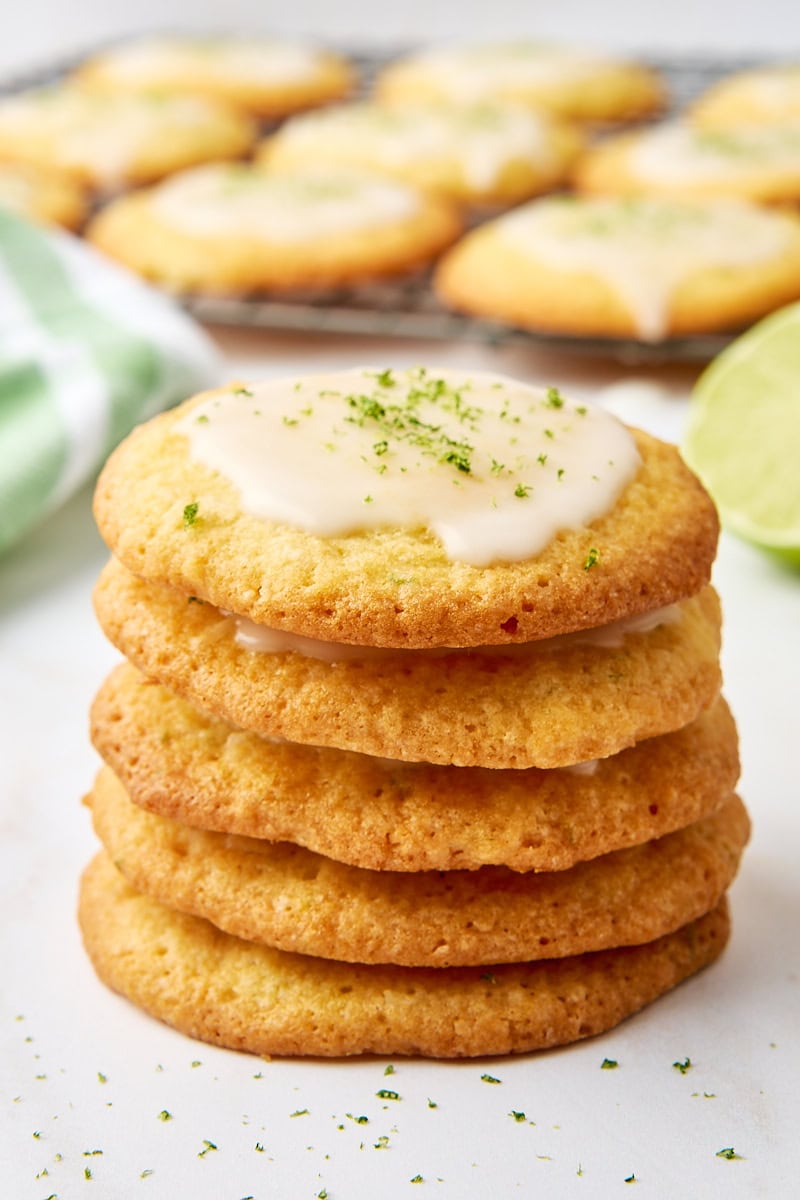 stack of five coconut lime cookies with more cookies on a wire rack in the background