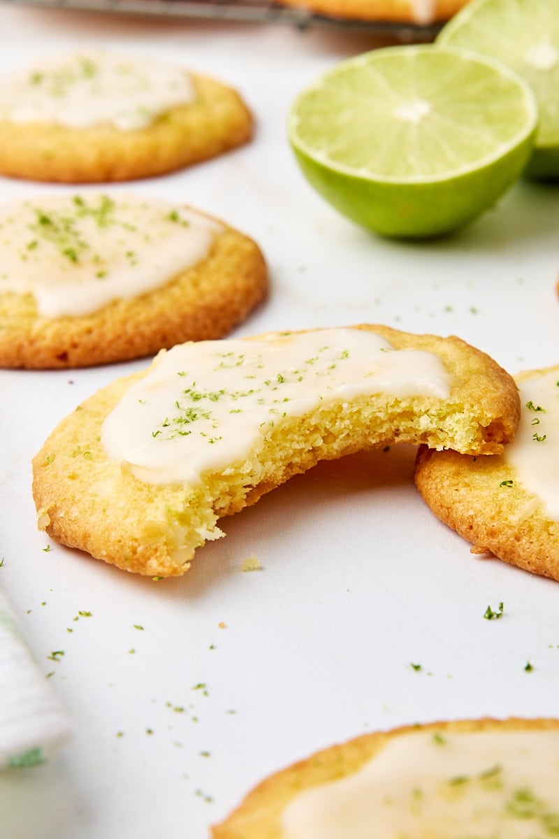 a coconut lime cookie with a bite missing, surrounded by more cookies and sliced limes