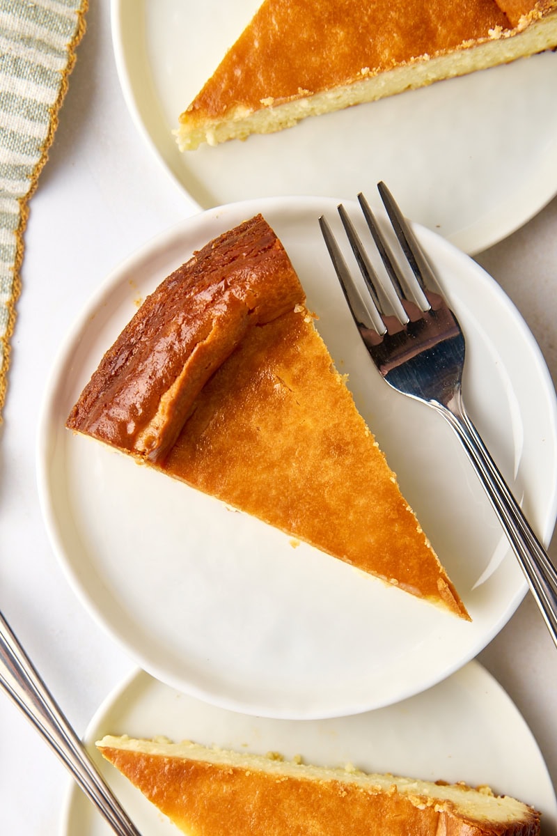 overhead view of a slice of New York cheesecake on a white plate with two more slices partially visible