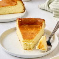 a slice of New York cheesecake on a white plate with a bite on a fork