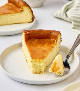 a slice of New York cheesecake on a white plate with a bite on a fork