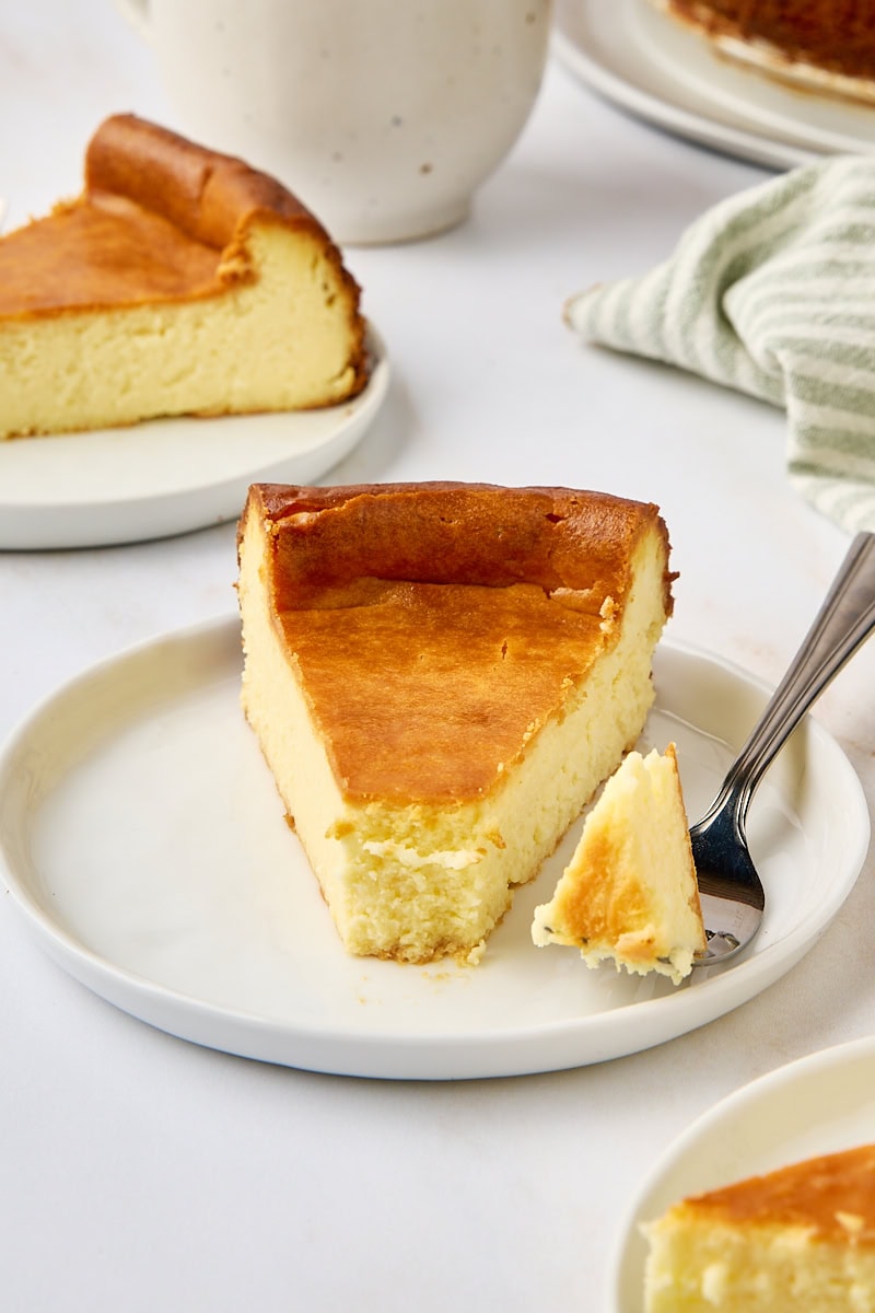 a slice of New York cheesecake on a white plate with a bite on a fork
