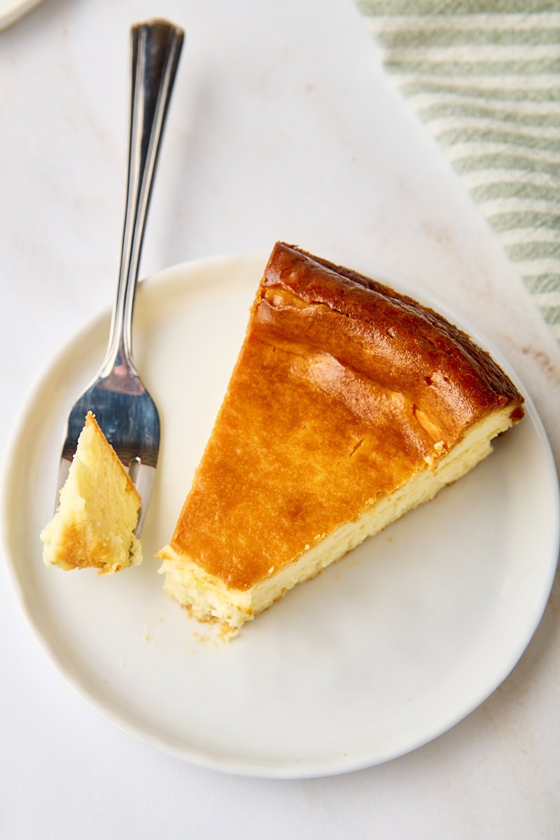 a slice of New York cheesecake on a white plate with a bite on a fork