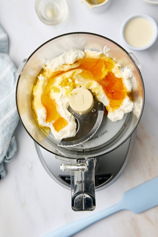 overhead view of ricotta, honey, vanilla extract, lemon zest, and salt in the bowl of a food processor