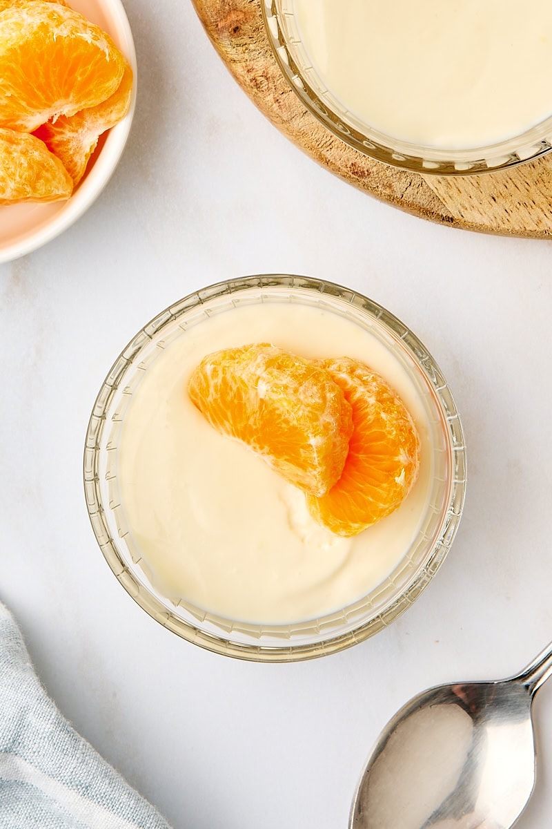 overhead view of a serving of ricotta mousse topped with two mandarin slices; more servings, mandarin slices, and a spoon partially visible
