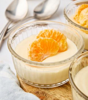 ricotta mousse in a clear glass ramekin topped with mandarin slices; more servings and spoons partially visible
