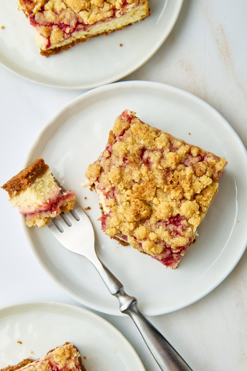 overhead view of a strawberry cheesecake bar on a white plate with a bite on a fork; more servings partially visible above and below