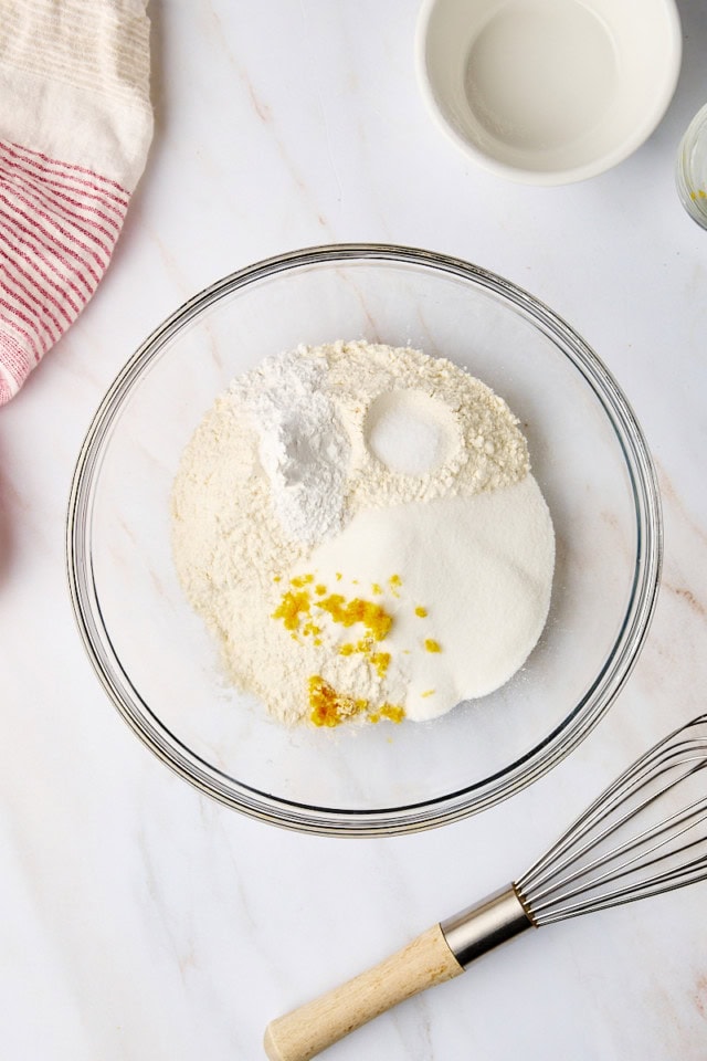 overhead view of flour, sugar, baking powder, salt, and lemon zest in a glass mixing bowl