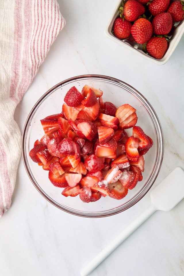 overhead view of strawberries, sugar, and lemon juice in a glass mixing bowl