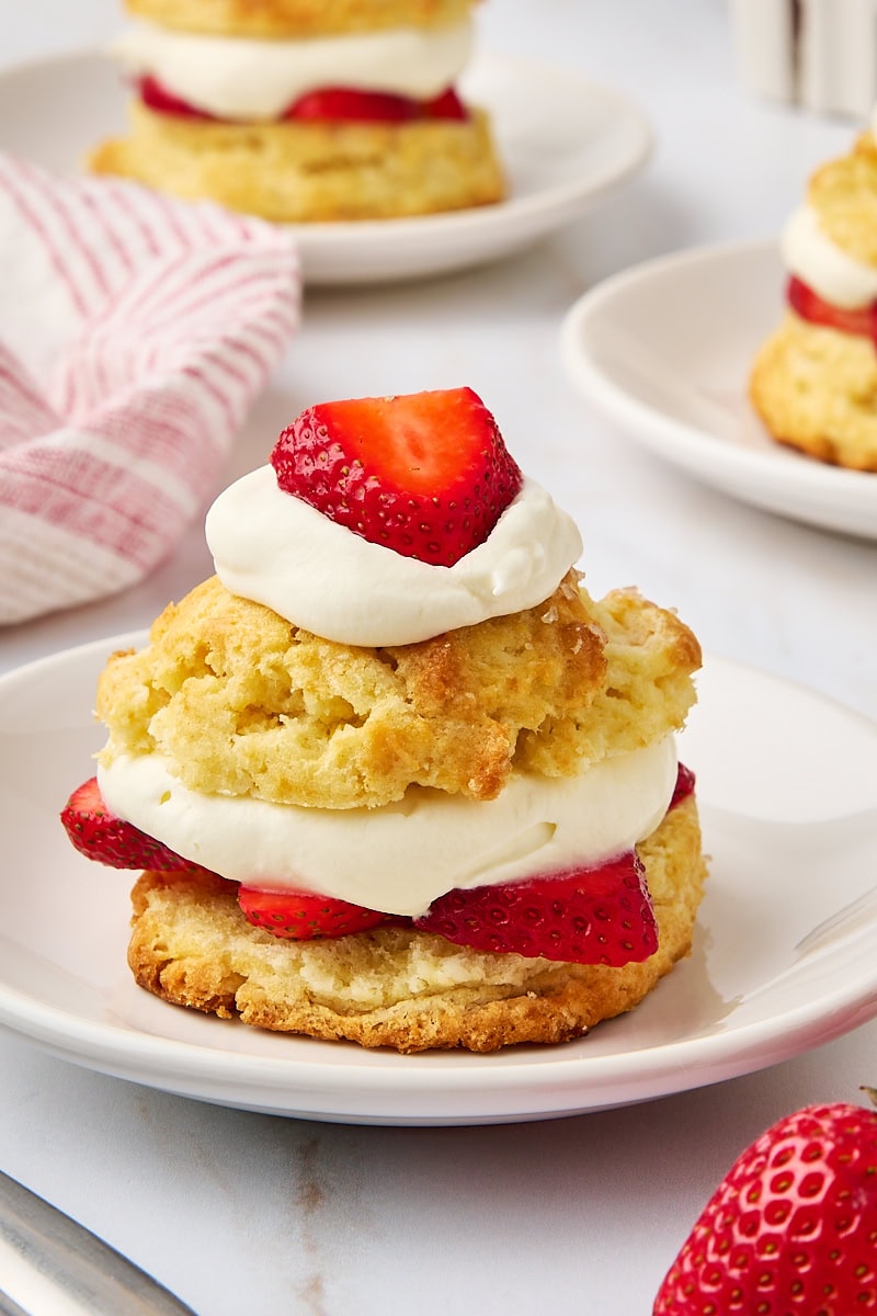 a strawberry shortcake on a white plate with two more shortcakes partially visible in the background