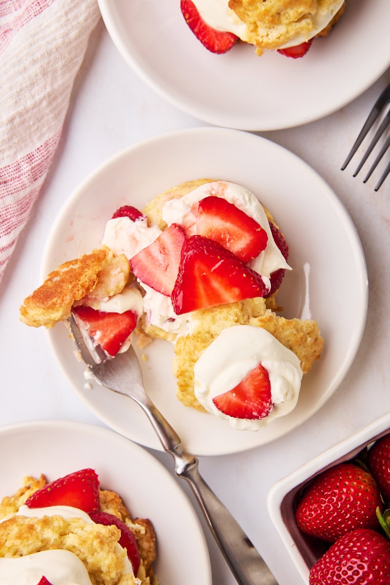 overhead view of strawberry shortcake on a white plate with a bite on a fork