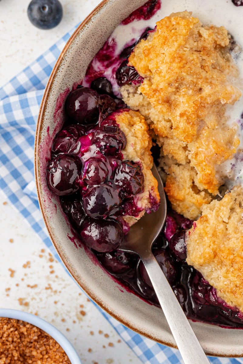 overhead view of a bowl of blueberry cobbler with a spoonful resting in the bowl
