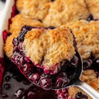 a spoonful of blueberry cobbler with remaining cobbler in the background